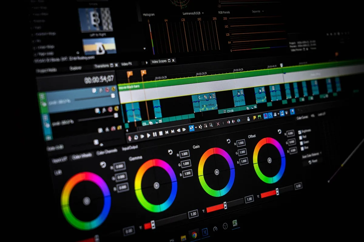 A colorist adjusting color wheels on a monitor showing a film scene in a dark editing suite.